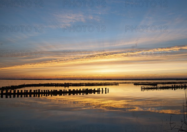 Sunset over water with impressive sky and light reflections, wooden posts reflected in the water,
