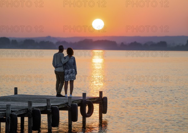 A couple stands on a jetty and looks at a colorful sunset over Lake Dümmer, Lembruch, Dümmer nature