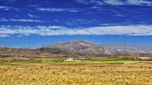Wide fields in front of a mountain range under a cloudy sky, The Altiplano landscape in the Andes