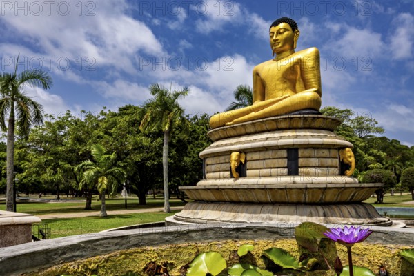 Close-up view of a golden Buddha statue with lotus flower surrounded by palm trees and blue sky,