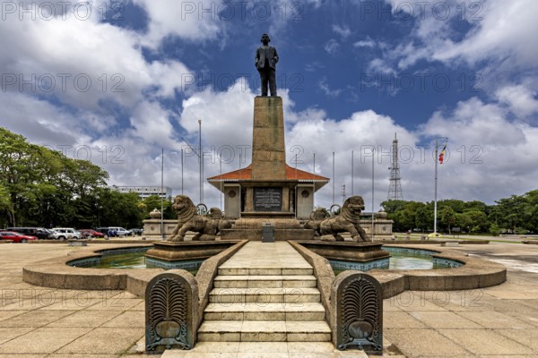 A monument with a statue on a pedestal surrounded by lions and a fountain on a cloudy day, Colombo