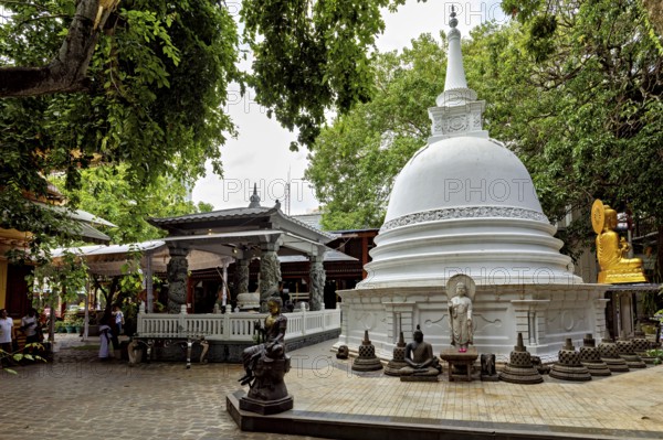 A Buddhist temple complex with a white stupa surrounded by Buddha statues and lush greenery, The