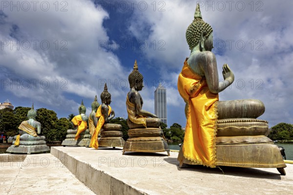 Buddha statues on the water with yellow robes against an urban backdrop, The Seema Malaka Temple