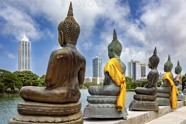 Buddha statues in bronze with yellow cloths in front of skyscrapers and water, The Seema Malaka