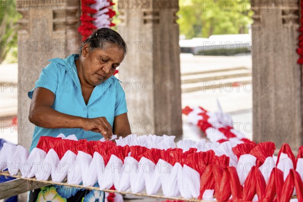 Woman making red and white decorations in an enclosed space, people making garlands in Colombo Sri