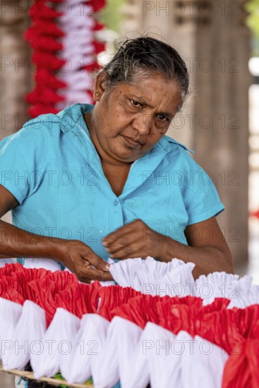 Woman concentrates making red and white decorations, people making garlands in Colombo Sri Lanka
