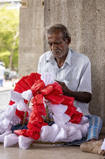 Elderly man sitting and concentrating making flowers, people making garlands in Colombo Sri Lanka