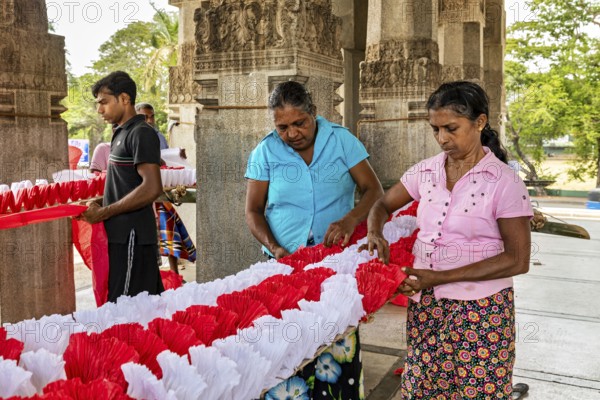Women making traditional decorations in a temple-like building, people making garlands in Colombo