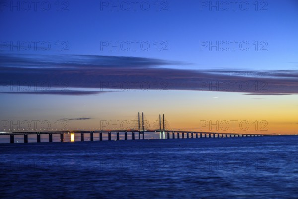 Modern Øresund bridge across the sea at sunset with colorful sky illuminated by a colorful sunset,