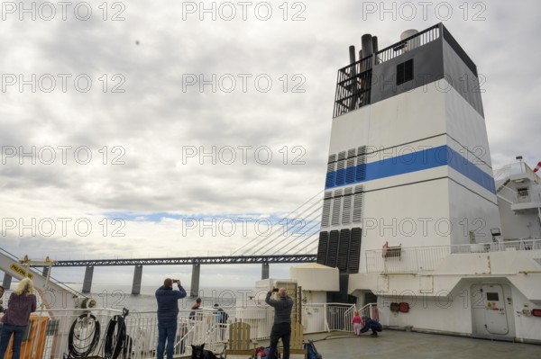 Passengers on a ship with a view of the Øresund Bridge, a ferry under a massive bridge structure of