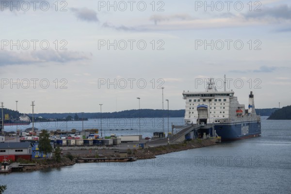 Large ferry in Naantali harbor on the water, surrounded by various buildings and a cloudy sky,