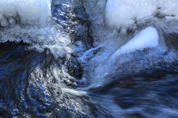Ilsenburg, Saxony-Anhalt, Germany, Flowing water breaks through thick layers of ice in winter on