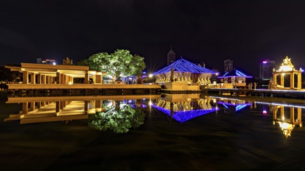 Nocturnal scene with illuminated pavilions, reflections in the water and city in the background,