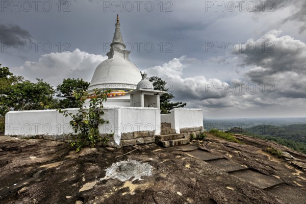 White stupa on rocky hill surrounded by cloudy skies and lush nature, The Maligatenna Purana