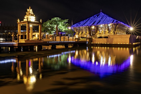 Night scene of an illuminated temple whose lights are reflected in the water, The Seema Malaka