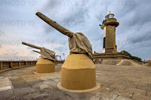 A lighthouse next to two cannons on a paved area under a cloudy sky, The Colombo Sri Lanka