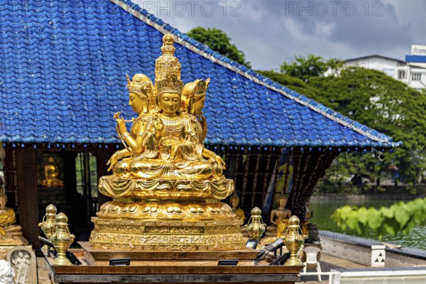Golden Buddhist statue in front of a blue roof with cloudy sky, The Seema Malaka Temple with the
