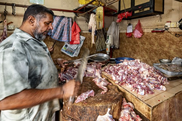 A butcher shreds pieces of meat with a cleaver on a wooden table in a traditional market