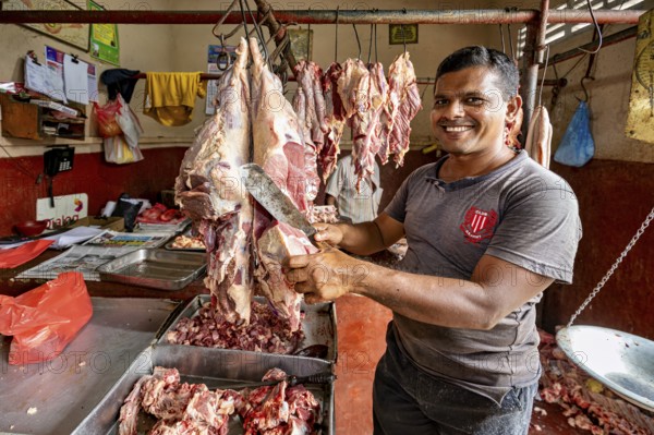 A smiling butcher cuts meat in a traditional shop, with pieces of meat around him, butcher shop in
