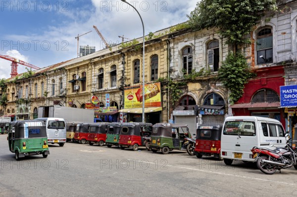 Busy urban street with old buildings and a series of tuk-tuks including a cloudy sky, tuk tuk in