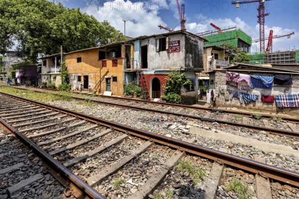 Construction cranes rise behind brightly painted houses along the train tracks under a blue sky,