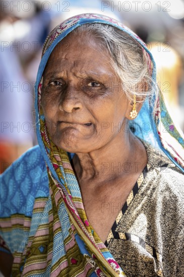 Elderly woman wearing a blue sari with a serious expression and traditional jewelry, portrait of an