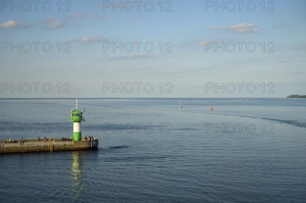 A green lighthouse harbour fire stands on a pier at the port exit of Travemünde in front of a calm,
