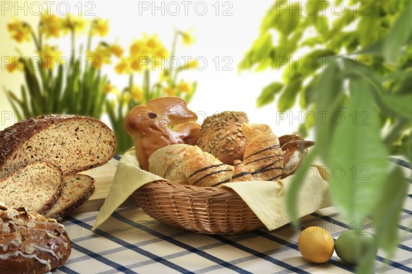 Easter basket with pastries, bread, Easter eggs, on checkered tablecloth, plants and flowers as
