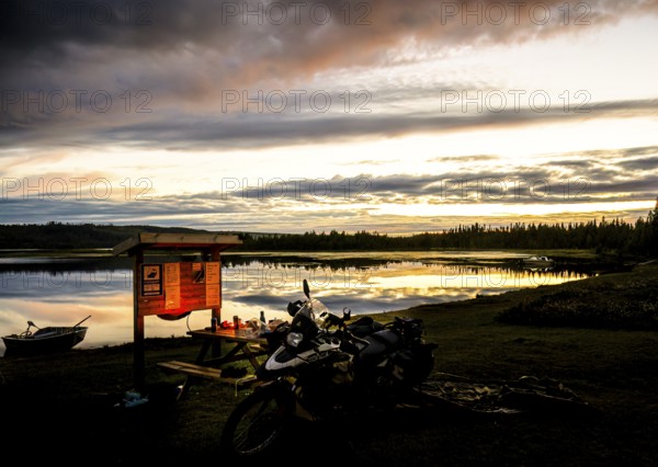 A BMW model G 650 GS Sertao motorcycle stands in front of a lake at sunset with dramatic clouds in