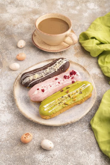 Glazed Eclairs on brown concrete background and green linen textile, cup of coffee, side view,