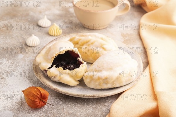 Glazed Pies with blueberry jam on brown concrete background and orange linen textile, cup of
