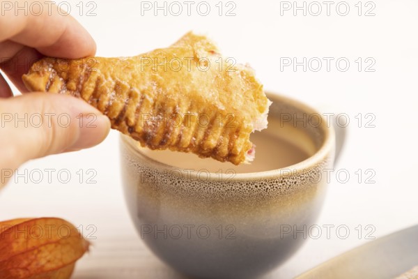Triangles Pie, Puff Pastry, Samsa with cherry jam with hand on white wooden background, cup of