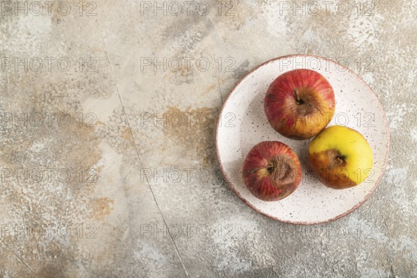 Decaying, Rotting apples on ceramic plate on brown concrete background. Top view, copy space, flat