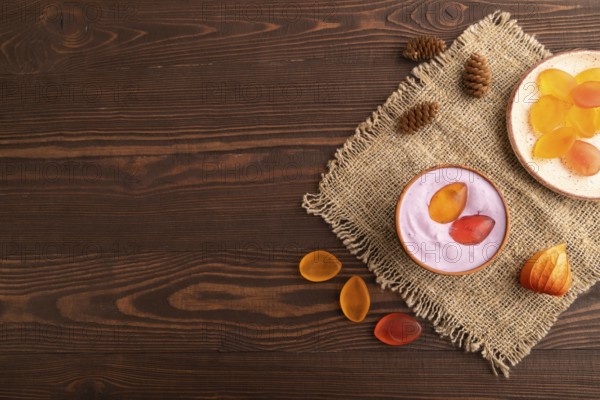 Purple Yogurt, with jelly candy on brown wooden background and linen textile, top view, flat lay,