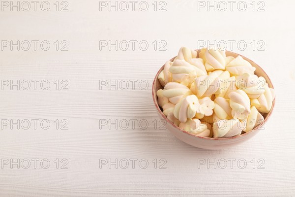 Orange and pink marshmallow in ceramic bowl on white wooden background, side view, copy space,