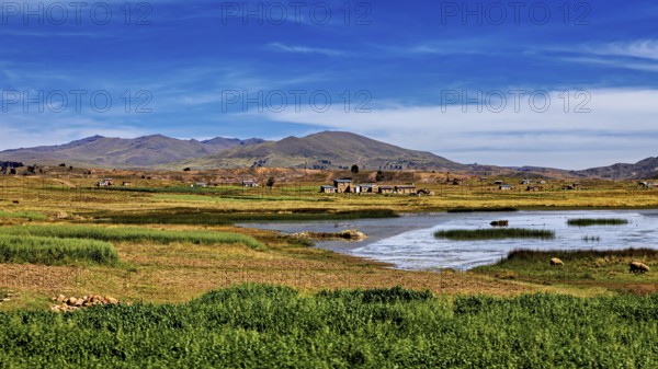 Wide landscape with a lake surrounded by meadows and small villages under a blue sky, The landscape