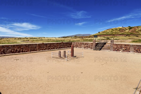 A rectangular square with stone pillars surrounded by ruins under a clear sky, The archaeological