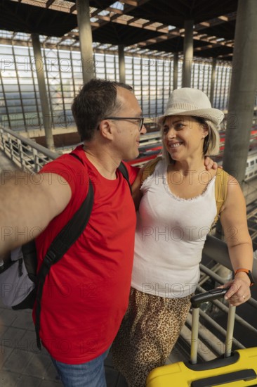 Smiling adult travel couple taking a selfie while looking at each other inside a modern train