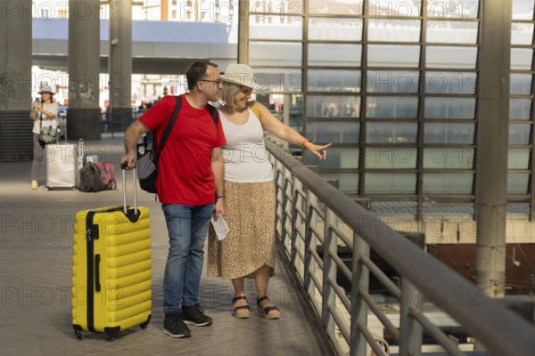 Adult travel couple walking together inside a modern transportation terminal above train tracks,