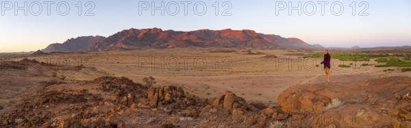 Young woman standing in desert landscape with Brandberg in morning light, at sunrise, Erongo,