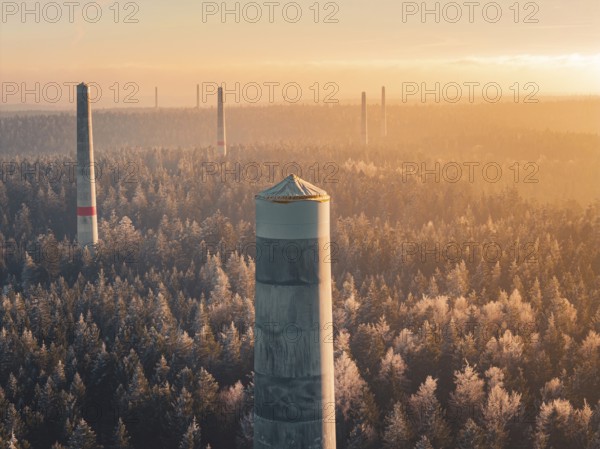 Wind turbine towers stand in orange light in the morning over a forest surrounded by thick fog, a