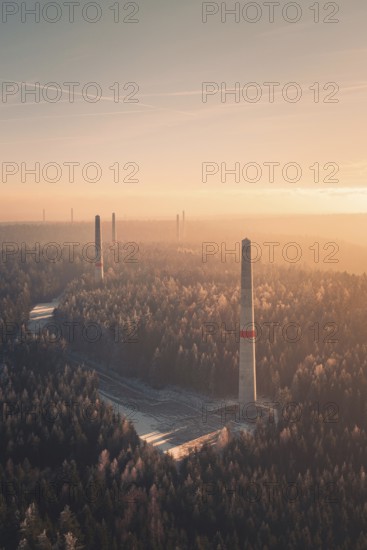 Wind turbine towers tower above a forest at sunset, soft pastel colors and fog create a quiet