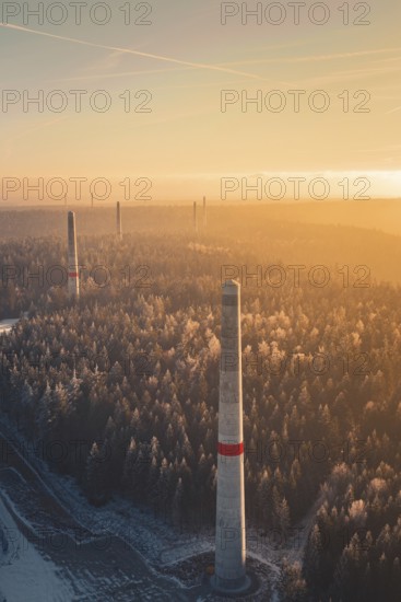 Wind turbine towers over a forest criss-crossed with snow trails, in warm sunlight, create a