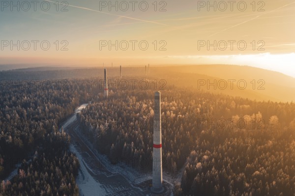 Sun rays over a foggy forest and wind turbine towers rising from the tree cover, Windkraft Bau,