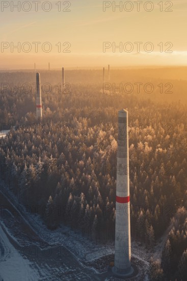 Wind turbine towers over snow-covered trees, the warm light and the fog create a mystical scene