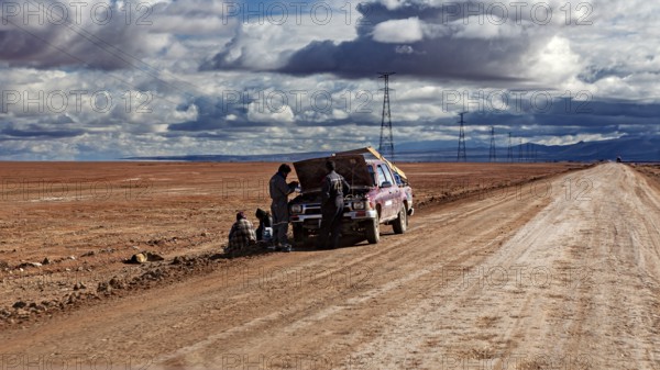A car is being repaired on the side of the road by several people in the desert, The landscape of