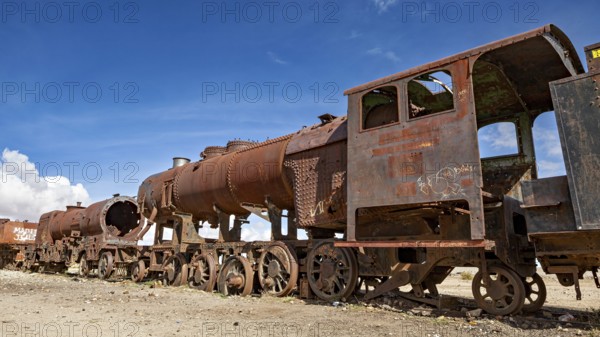 Long line of rusty locomotives in an open desert landscape under clear skies, old rusty locomotives