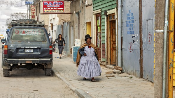Woman wearing traditional clothes wearing melon walks on a sidewalk with colorful houses and