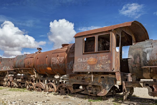 Rusty locomotive with vivid graffiti against a blue, cloudy sky, old rusty locomotives at the train