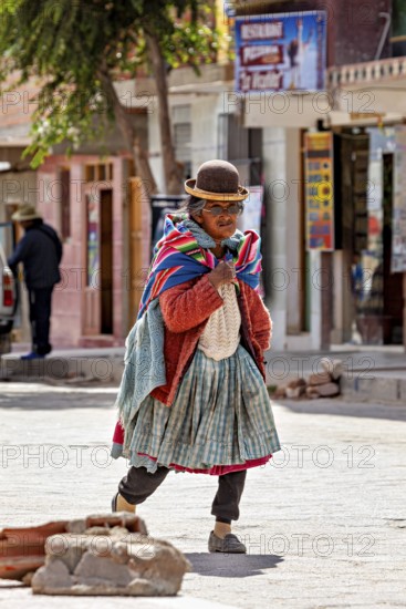 Elderly woman in traditional clothes with melon and colorful scarf walks on cobblestone street,